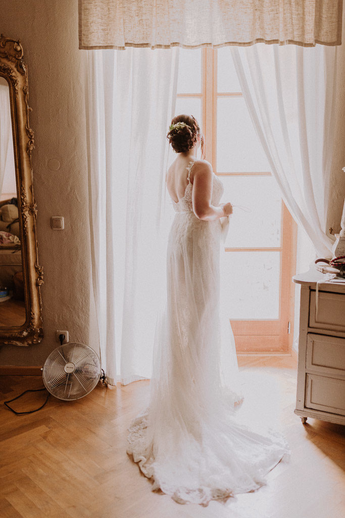 Braut blickt mit ihrem Brautkleid durch das große Fenster des Schlosses