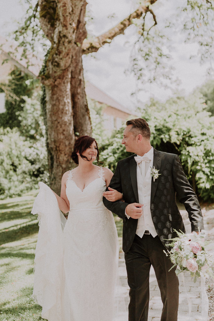 Brautpaar schreitet glücklich und sich anlächelnd im Schlossgarten Amerang entlang