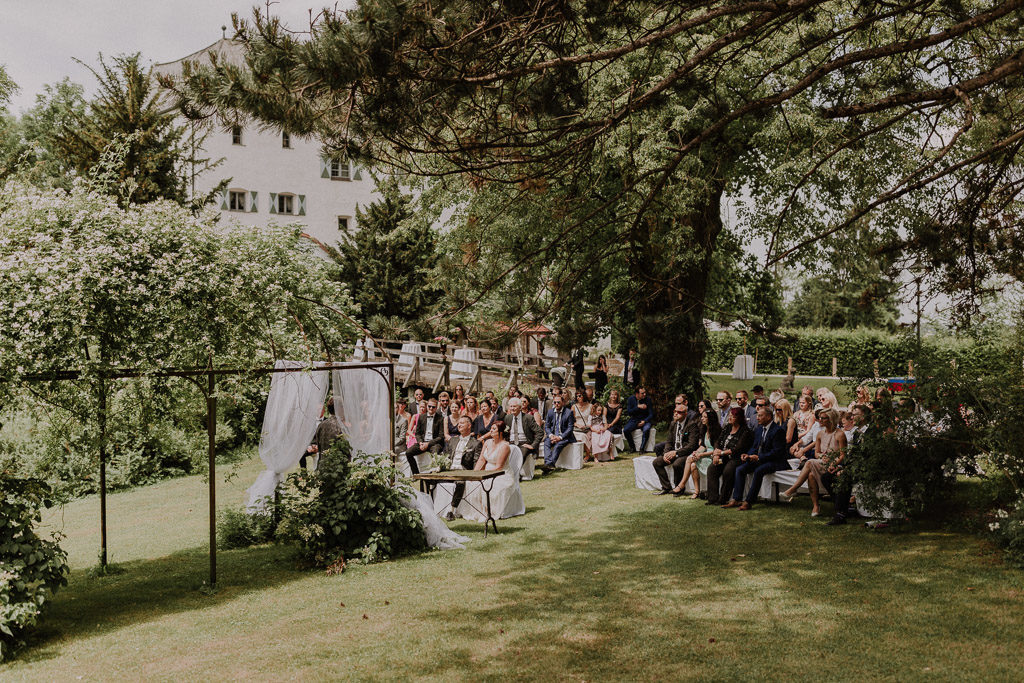 Die freie Trauung mit Hochzeitsgästen im Schlossgarten umgeben von Bäumen und Sträuchern